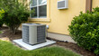 © EPICreation - A modern residential air conditioner unit on concrete pad, green bushes surrounded exterior condenser HVAC, beige house wall background - home comfort, cooling technology for summer heat concept