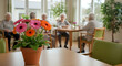 © EPICreation - Colorful flowers in pot, assisted living community common area background with engaged residents interact in warm space - senior activity, social interaction, care, and joyful togetherness