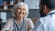 © Johannes - happy older mature female patient talking to indian male doctor at appointment healthy smiling senior old woman feeling cheerful about good news at medical consultation elderly health medical care no