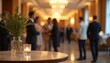 © Raisa - Blurred image of business conference event in luxury hotel hall. People near table with candle, plant. Warm lighting from chandeliers, lamps creates inviting atmosphere for networking, formal