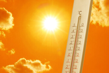 Wall Mural - thermometer showing high temperature against orange sky with bright sun and clouds. extremely hot we