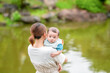 © Masakazu Tokashiki - A woman holds a baby in her arms while standing by a body of water. Concept of calm and serenity, as the mother and child enjoy the peaceful surroundings