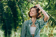 © SHOTPRIME STUDIO - Bright portrait of a smiling woman outdoors among lush greenery, wearing a striped green shirt and white top, bathed in warm sunlight.