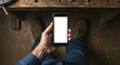 © Cleverson - Person holding a smartphone with a blank screen while sitting at a workbench, showing technology and potential use in manual work.