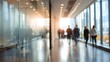 © pingpao - A blurred office corridor with people walking, illuminated by natural light from large windows, creating a dynamic and busy atmosphere.