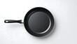 © sofyan - High-angle, top-down view of a black frying pan on a white surface. The pan is round, with a smooth, dark interior and exterior.  A silver-colored handle extends from the pan, with a black grip