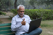 © Pix4Ads - Indian senior man showing thumbs up while working on laptop at park