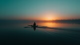 A lone rower glides silently across a calm lake, silhouetted against a vibrant sunrise, capturing tranquility and solitude.