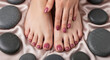 © MIQ - Close-up of a woman's perfectly manicured feet and hands adorned with deep rose nail polish, surrounded by smooth, dark spa stones on a lustrous satin fabric.