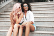 © halayalex - Two young beautiful smiling female in trendy summer clothes.Sexy carefree multiracial women posing on the street background.Positive models in sunglasses. Cheerful and happy. Sitting at the stairs