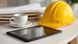 © Subin - A construction workspace featuring a tablet, hard hat, and coffee cup symbolizing modern work life balance.