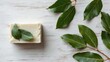 © Kahartakhassus - Natural soap bar surrounded by leaves on a white wooden surface