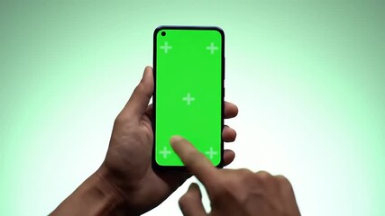 Close-up of a person's hand holding and tapping a modern smartphone with a blank green screen, showcasing interactive chroma green technology for digital mockups