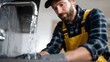 © Bussakon - A focused professional plumber wearing gloves works on a kitchen sink with water running from the faucet