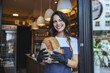 © Dragana Gordic - Smiling Woman Bakery Worker Holds Fresh Loaf at Cozy City Cafe Entrance