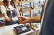 © Dragana Gordic - Smiling Cashier Hands Card Reader to Customer at Bakery Checkout in Busy Store