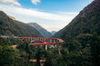 © Connect Images - A vibrant red bridge snakes through lush green mountains under a clear blue sky.  Kelok 9, or the 9 hairpins, Harau, West Sumatra, Indonesia