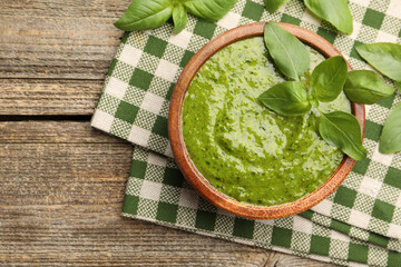 Wall Mural - Tasty green pesto in bowl and basil leaves on wooden table, top view. Space for text