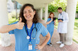 © StockMe - Healthcare worker smiling, giving thumbs up, showing approval and success with medical team members in background