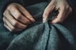 © hkjdesign - Close-up of hands skillfully sewing a dark-colored fabric using needle and thread.