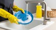 ©  AH Creation - Hands in yellow gloves washing a blue plate with soap and water in a sink