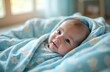 © Viktor - Newborn baby rests wrapped in blue star print sleep sack. Infant looks at camera from cozy nursery bed. Peaceful, safe sleep solution for young child.