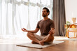 © Maria Vitkovska - Bearded, middle aged man practicing meditation indoors at home sitting in lotus position