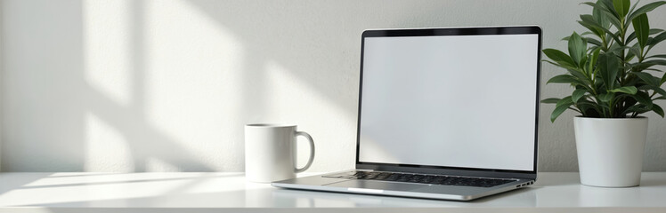 Modern laptop with blank screen sits on white desk next to coffee mug and green plant. Bright window light casts shadows on wall. Minimalist workspace setup for remote work.