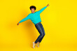 © deagreez - Energetic young man in a teal sweatshirt posing playfully against a vibrant yellow background expressing joy and style