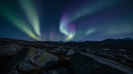 Wall Mural - glowing aurora borealis ribboning over barren rocky landscape under a darkened arctic sky timelapse 