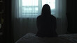 © SeM_Video - Back view Silhouette of a millennial woman sitting on a bed in the dark bedroom, depression, pain. Portrait of Unhappy sad woman sitting against window and thinking about her life