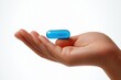 © oio - close up of a hand holding a single blue capsule pill on an open palm against a white background conveying health and medicine