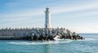 © ALLmost - A white lighthouse stands tall on a breakwater made of concrete tetrapods, with waves crashing against the shore under a clear blue sky.