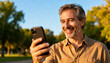 © BrunoStudio - Mature handsome man smiling during a video call on his smartphone in the park. Happy middle-aged person using technology for communication and staying connected with family.