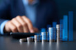 © Secrets inside - Stacks of coins arranged in ascending order with a blurred person using a calculator in the background, symbolizing financial growth and investment analysis