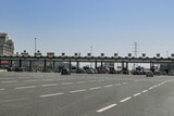 A wide shot of a multi-lane toll plaza on a highway in Portugal. Cars are visible in the lanes, with a large overhead structure of signs and lights.