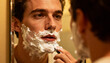 © Hellena - Morning self-care ritual. Man applying shaving cream foam in front of a mirror. Grooming and hygiene routine. Skincare concept for men. Close-up face with razor for a clean shave.