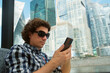 © familylifestyle - Man tourist looking at smartphone sitting in river tram public transport in city. Reading news, surfing online, chatting in mobile phone. Modern skyscrapers cityscape on background in window.