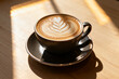 © Big - A cup of latte with leaf-patterned foam art on a wooden table illuminated by sunlight
