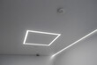 © fototema - A photo showing a minimalist ceiling design with modern lighting. The main focus is on the recessed rectangular LED strip and the long linear lighting running along the wall.