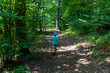 © Maryia - Child in blue shirt walking with stick on forest path surrounded by lush green trees on sunny day. Concept of outdoor exploration, nature adventure and healthy childhood activities.