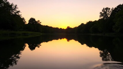 Wall Mural - ﻿slow cinematic dolly shot across a tranquil pond surface reflecting golden hour light and distant t