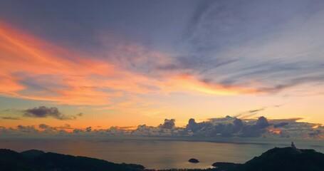 Wall Mural - A breathtaking sunset paints the sky in vivid hues of orange and blue over a coastal town, with lush green hills framing the scene. A distant hilltop structure adds a serene focal point to landscape.