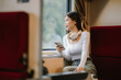 © Worawi - Asian woman sitting at a railroad station with backpack, using mobile phone and laptop, waiting for train, enjoying travel lifestyle.