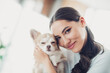 © deagreez - Beautiful woman embracing her adorable small dog while enjoying a relaxing moment indoors during daylight.