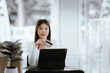 © Witoon - Young woman holding credit card and smartphone, making online payment while using laptop in modern cafe.