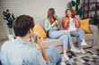© deagreez - Group of young friends enjoying a casual conversation at home while sharing drinks in a relaxed living room setting