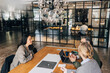 © Maskot - High angle view of smiling female giving interview to business professionals while sitting at table in office