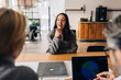 © Maskot - Happy woman giving interview to business experts while sitting at table in office