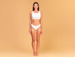 © Prostock-studio - Full length frontal view of slim woman with perfect body shape and flat tummy posing on beige studio background, lady wearing white lingerie, copy space